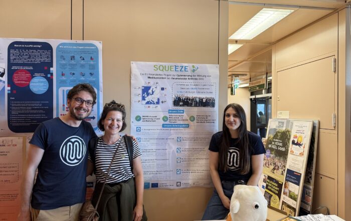 Three people in front of a SQUEEZE poster