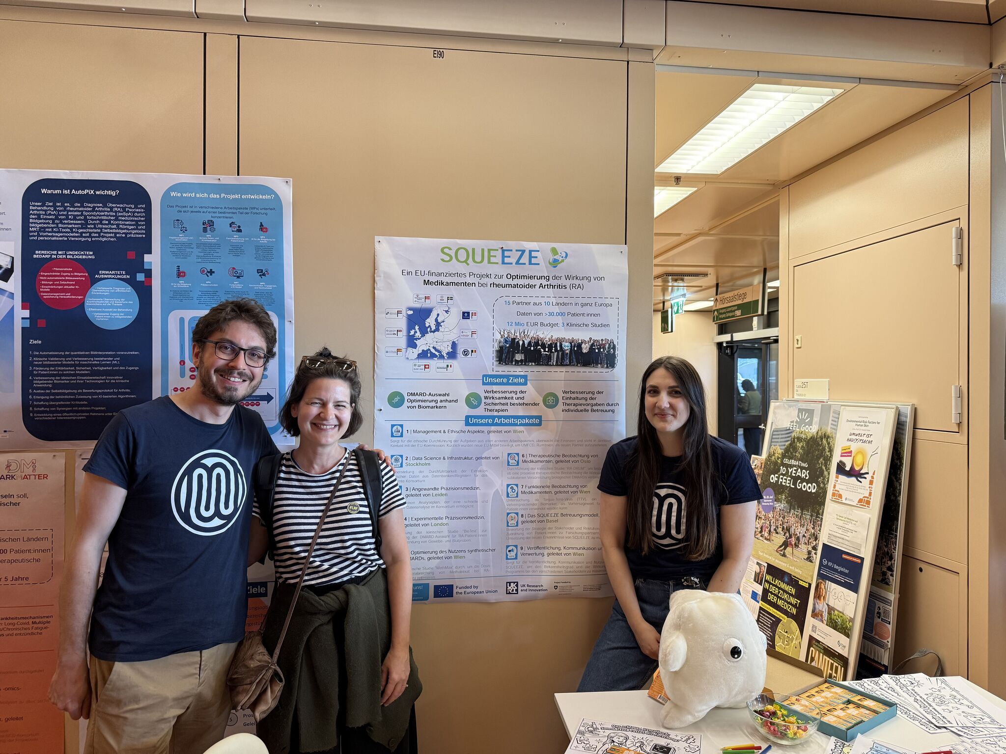 Three people in front of a SQUEEZE poster