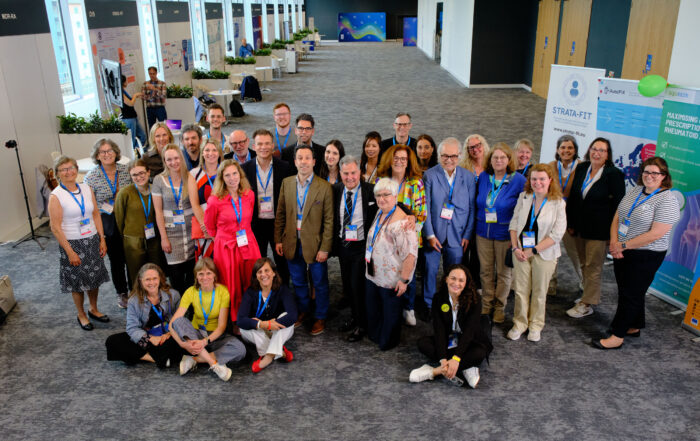 A group of people, smiling into the camera. In the background a conference setting
